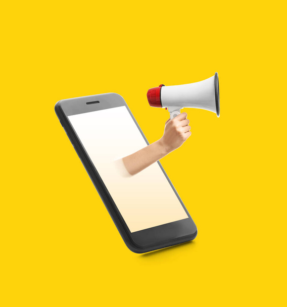Mobiele telefoon en hand met megafoon op gele achtergrond - Foto, afbeelding