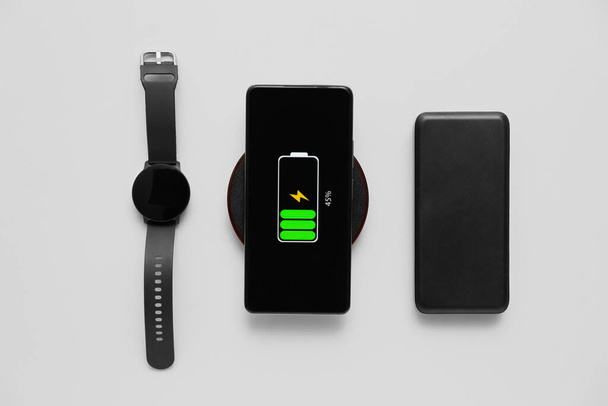 Carregamento de telefone móvel moderno com almofada sem fio, smartwatch e banco de energia em fundo cinza - Foto, Imagem
