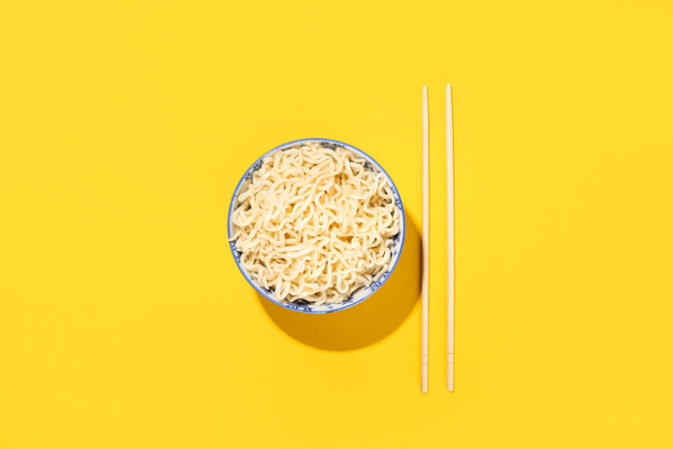 Bowl with tasty noodles and chopsticks on yellow background - Foto, imagen