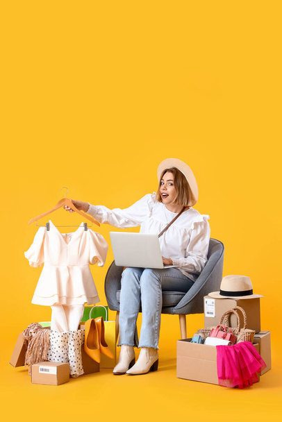 Sarı arka planda dizüstü bilgisayarı ve alışveriş çantaları olan genç bir kadın. - Fotoğraf, Görsel