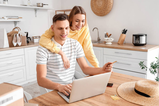 Junges Paar mit Laptop und Kreditkarte kauft online in Küche ein - Foto, Bild