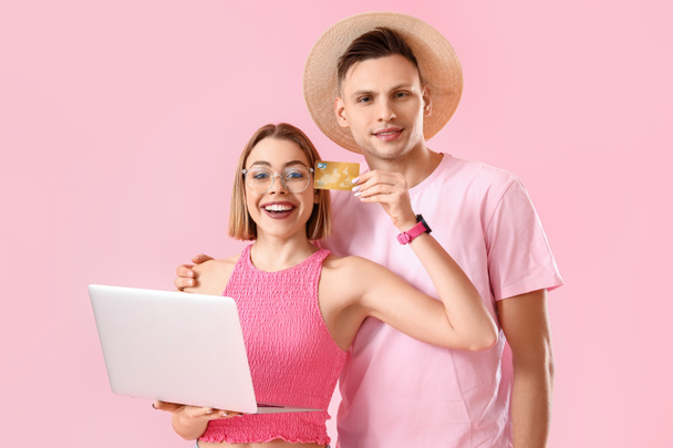 Young couple with laptop and credit card on pink background. Online shopping - Fotografie, Obrázek