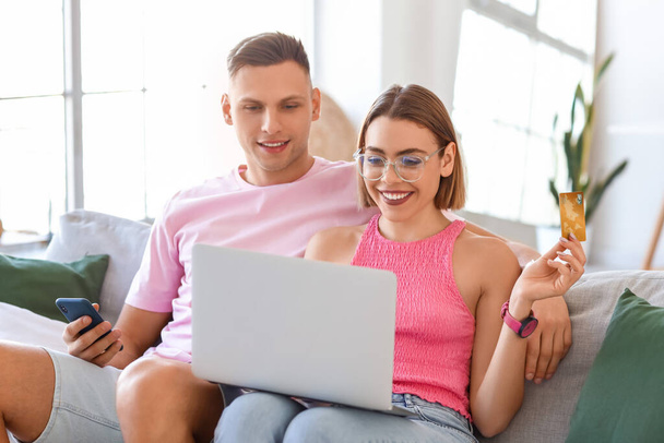 Νεαρό ζευγάρι με φορητό υπολογιστή, κινητό τηλέφωνο και πιστωτική κάρτα στο σπίτι. Online αγορές - Φωτογραφία, εικόνα