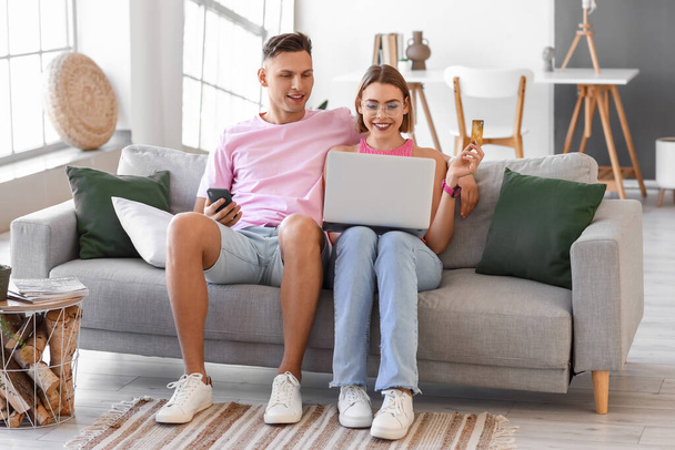 Junges Paar mit Laptop, Handy und Kreditkarte zu Hause. Online-Einkauf - Foto, Bild