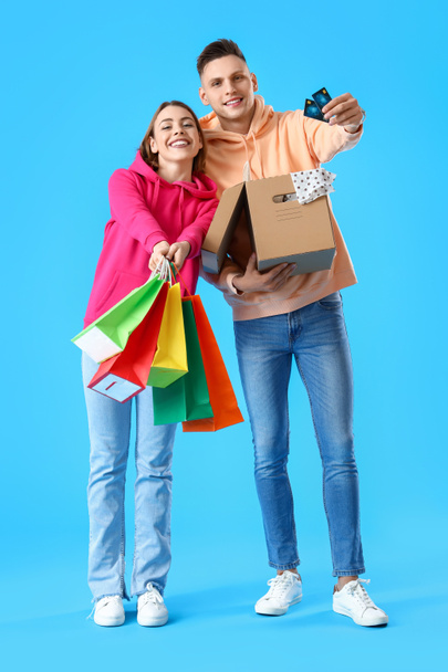 青の背景にクレジットカード、ショッピングバッグや小包を持つ若いカップル - 写真・画像