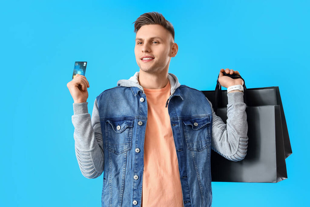 Молодой человек с сумками и кредиткой на синем фоне - Фото, изображение
