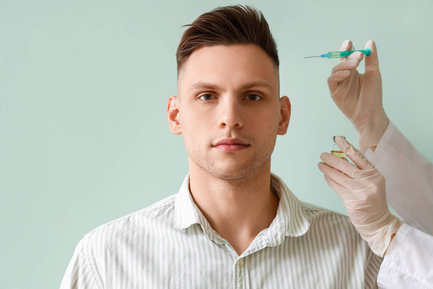 Молодой человек с проблемой выпадения волос получает инъекцию на зеленом фоне - Фото, изображение
