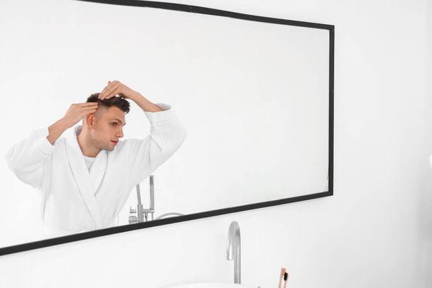 Mladý muž s problémem vypadávání vlasů v blízkosti zrcadla v koupelně - Fotografie, Obrázek