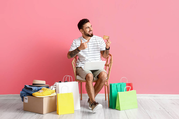 Handsome man with laptop pointing at credit card on pink background. Online shopping - Foto, immagini