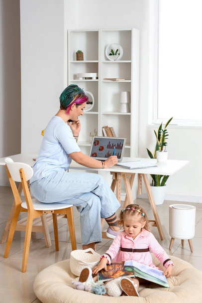 Klein meisje met boek en haar werkende moeder thuis - Foto, afbeelding