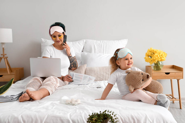 Cute little girl with toy and her working mother in bedroom - Fotoğraf, Görsel