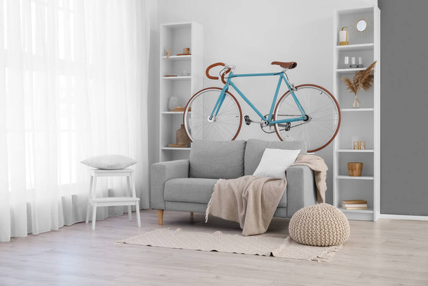 Innenraum helles Wohnzimmer mit Fahrrad, grauem Sofa und Regalen - Foto, Bild