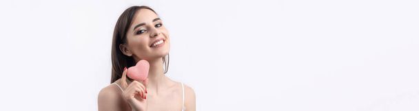 Schöne lächelnde Frau mit sauberer Haut, natürlichem Make-up und weißen Zähnen auf grauem Hintergrund. Ein rosafarbenes, hygienisches Herz. - Foto, Bild