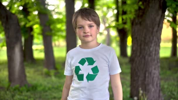 Muchacho con guantes de goma mostrando como en la recolección de basura de plástico en un parque contaminado, reciclando letrero en la camiseta. Movimiento lento - Imágenes, Vídeo