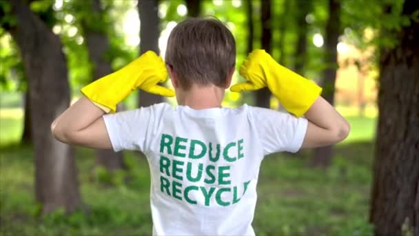 Niño con guantes de goma mostrando en la inscripción ecológica en su camiseta. Recogida de basura plástica en un parque contaminado. Movimiento lento - Metraje, vídeo