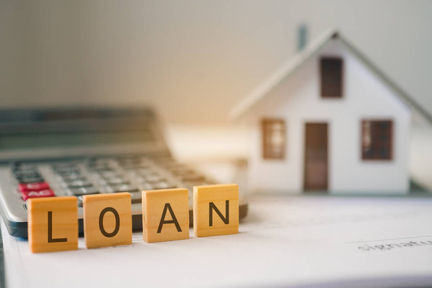 Casa modelo con letras "LOAN" talladas en bloques de madera. El concepto de un contrato de préstamo inmobiliario, así como un préstamo inmobiliario. - Foto, Imagen