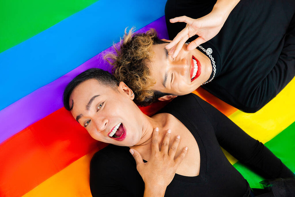 Foto von Happy asiatische homosexuelle Paar legen sich auf Stolz Flagge Regenbogenfarbe Hintergrund. lgbtq und lgbtq + Konzepte - Foto, Bild