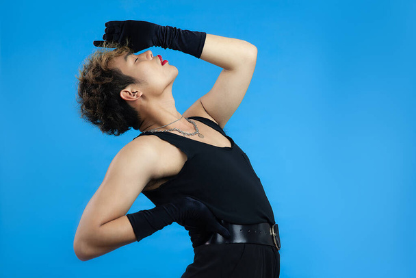 gay man with red lip stick and black tank top posing isolated blue background. Transgender Gay Pride LGBTQ+ concepts - 写真・画像