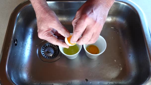 Egy férfi feltöri a tojást a mosogatóban, hogy elválassza a fehéreket a sárgájától..  - Felvétel, videó