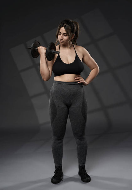 Strong size plus indian woman doing fitness workout with weights, on grey background - Φωτογραφία, εικόνα