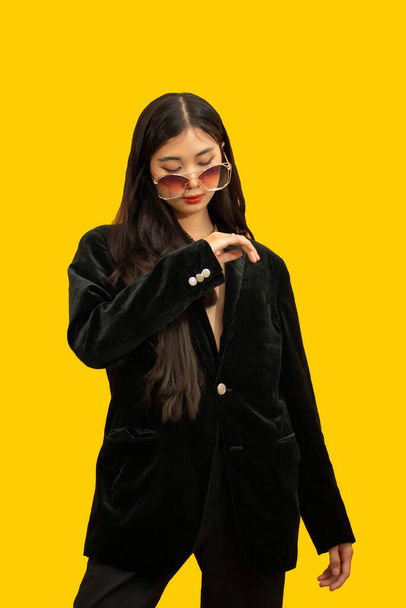 Koncepcja mody, Modna kobieta pozująca w czarnych strojach z okularami przeciwsłonecznymi na żółtym tle. - Zdjęcie, obraz