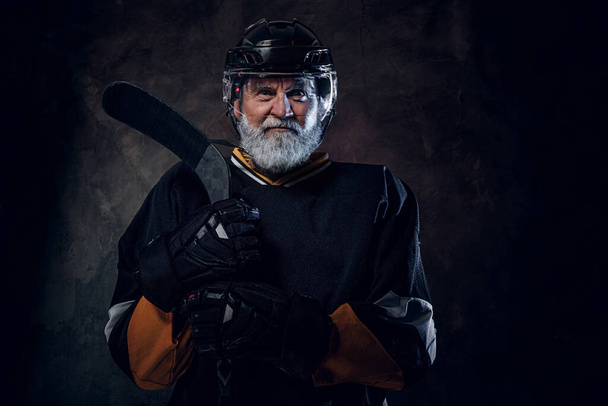 Выстрел активного старшего хоккеиста, одетого в защитную спортивную форму, держащего хоккейную клюшку. - Фото, изображение
