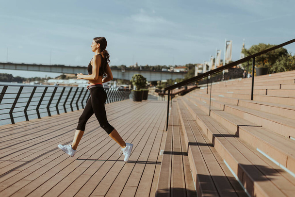 Pretty young woman in sportswear exercising on a river promenade - Photo, Image