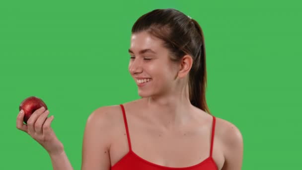 Портрет молодої щасливої жінки, яка тримає яблоньку, що виглядає зубатою, посміхаючись одягнутою червоною зверху здоровою дієтою концепт Ізольований на студії Green Screen - Кадри, відео