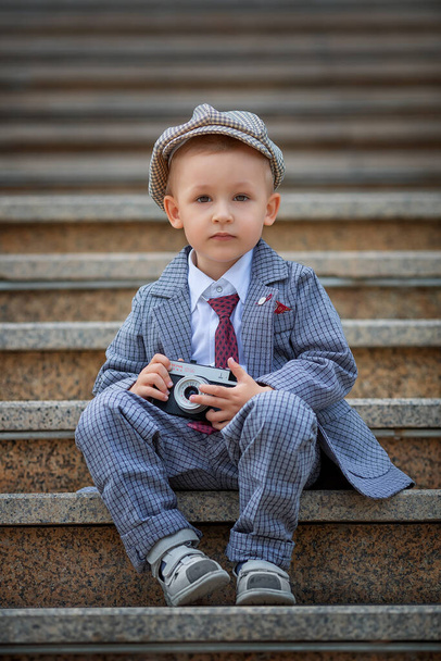 Portrait of a little kid boy photographer taking picture with retro vintage photo camera on the steps outside. Childrens photo shoot. People childhood lifestyle concept. - Фото, зображення