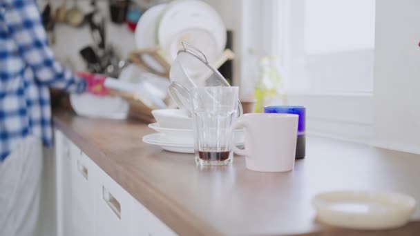 前景の汚れた皿の上に台所の洗面台の近くに立つ女性を背景に料理をする主婦 - 映像、動画