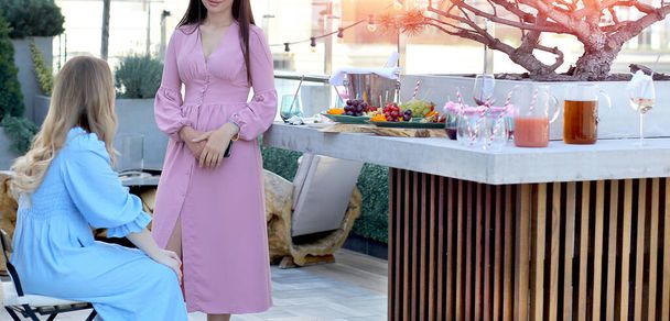 Banner with a girl in a pink dress at an event is talking to her friend. Background - the roof of the penthouse, fruits and drinks. Buffet, Party, meeting, holiday. - Foto, imagen