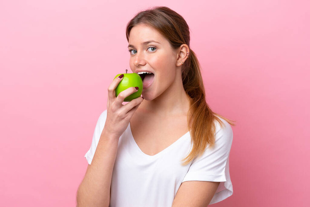 Young caucasian woman isolated on pink background eating an apple - Photo, Image