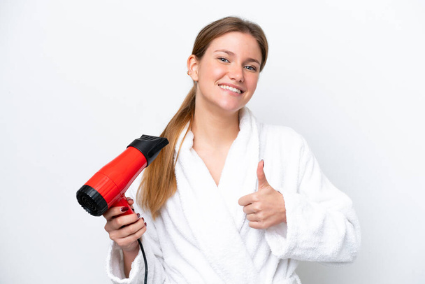 Young caucasian woman holding hairdryer isolated on white background with thumbs up because something good has happened - Photo, image