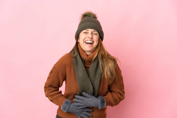 Keski-ikäinen nainen talvella hattu eristetty vaaleanpunainen tausta hymyilee paljon - Valokuva, kuva