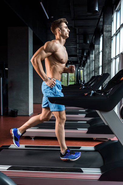 Young muscular adult man running on treadmill in gym. The athlete is in good shape. Personal trainer. Motion blur - Photo, Image