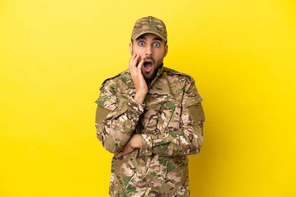 Wojskowy człowiek odizolowany na żółtym tle zaskoczony i zszokowany patrząc w prawo - Zdjęcie, obraz