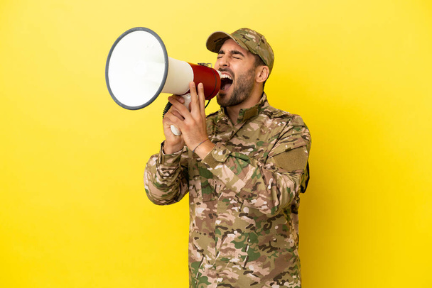 Στρατιωτικός άνδρας απομονωμένος σε κίτρινο φόντο φωνάζοντας μέσα από ένα μεγάφωνο - Φωτογραφία, εικόνα
