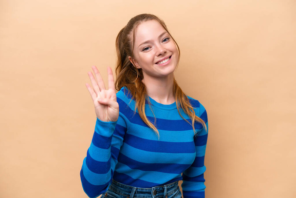 Νεαρή καυκάσια γυναίκα απομονωμένη σε μπεζ φόντο χαρούμενη και μετρώντας τέσσερα με δάχτυλα - Φωτογραφία, εικόνα