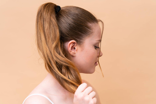 Young caucasian girl isolated on beige background touching her hair. Close up portrait - 写真・画像