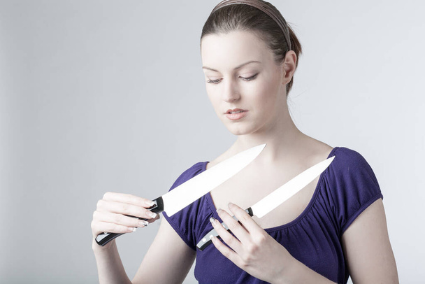 Eine junge Frau spielt mit zwei scharfen Küchenmessern  - Foto, Bild