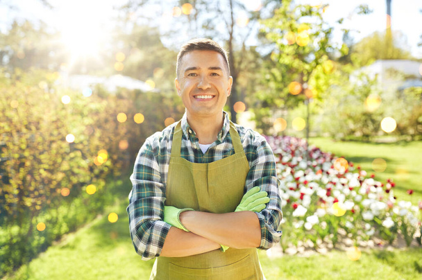 gardening and people concept - happy smiling middle-aged man in apron with crossed hands at summer garden - Фото, зображення