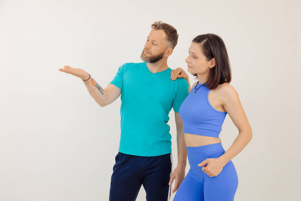 Young athletic woman and man in blue sportswear standing and pointing by hand, white background. Keeping fit by fitness workout in gym, pumping up body. Family sport and healthy lifestyle concept. - Photo, image