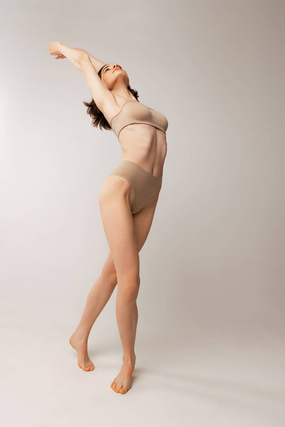 Full-length portrait of beautiful young woman posing in beige underwear isolated over grey studio background. Slim body. Concept of beauty, body and skin care, health, spa, wellness, cosmetics, ad - 写真・画像
