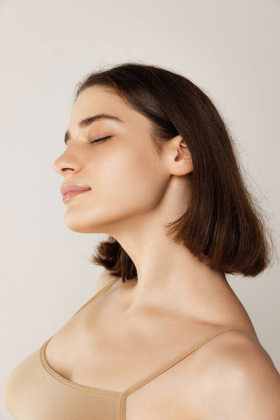 Close-up portret van jonge mooie vrouw poseren geïsoleerd over grijze studio achtergrond. Scherpe jukbeenderen. Concept van schoonheid, lichaams- en huidverzorging, gezondheid, kosmetologische behandeling, cosmetica, reclame - Foto, afbeelding