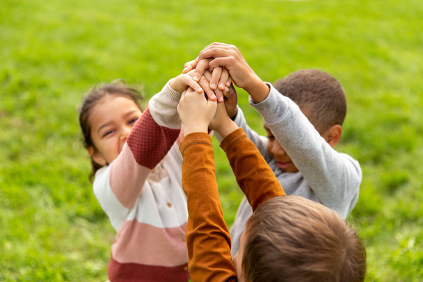 childhood, leisure and people concept - group of children stacking hands at park - Foto, Imagem