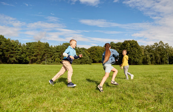 childhood, leisure and people concept - group of happy kids playing tag game and running at park - Foto, immagini