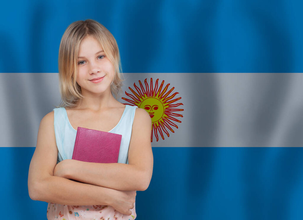 Cute young student girl with book on Argentine flag background. Education and school in Argentina concept. - Photo, Image
