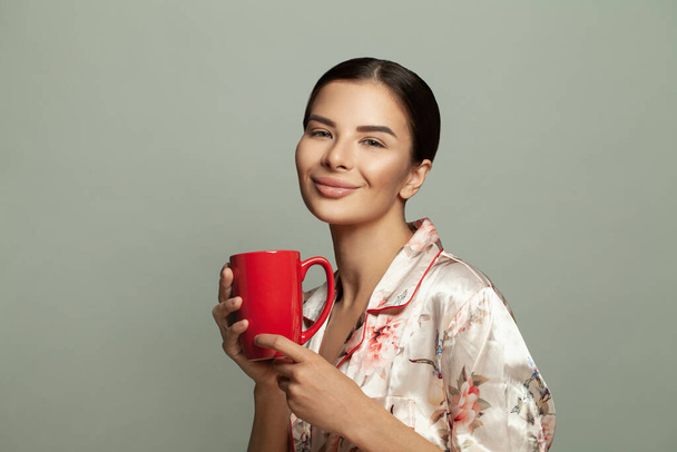 Beautiful sweet tender brunette woman holding red coffee mug on grey banner background - Photo, Image