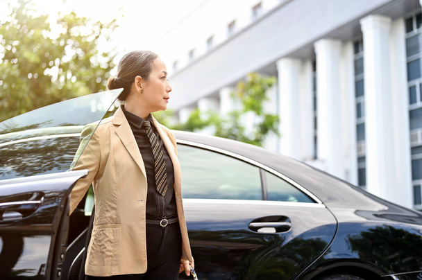Успішний азіатський керівник або старша бізнес-леді впевнено виходить з її розкішного автомобіля перед будівлею
. - Фото, зображення