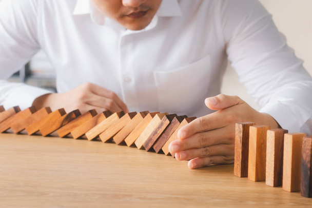 Risk management and business strategy concept, businessman hands stop the dominoes from falling continuously, preventing future risks from crisis. - Fotó, kép